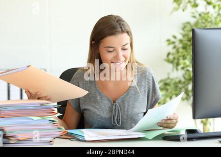 Felice dipendente per la gestione dei documenti in seduta una scrivania in ufficio Foto Stock