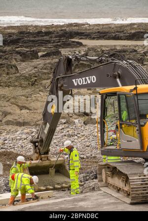 PORTHCAWL, GALLES - GIUGNO 2018: Operatori edili che spostano il calcestruzzo dal secchio di un escavatore per migliorare il lungomare di Porthcawl Foto Stock