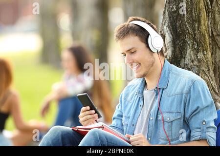 L apprendimento degli studenti in ascolto tutorials audio in un parco seduta sul prato di un parco Foto Stock