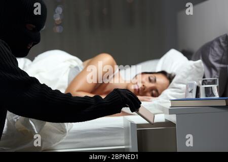 Ladro rubare un telefono la rottura in una camera da letto di una casa nella notte con una donna che dorme in background Foto Stock