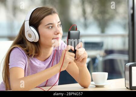 Single teen di indossare le cuffie per ascoltare la musica da un telefono intelligente in una caffetteria e terrazza Foto Stock