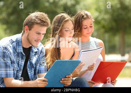 Tre studenti di concentrato di memorizzare note seduto in un parco del campus Foto Stock