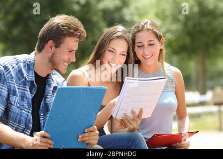 Tre felici gli studenti che studiano insieme confrontando le note in un parco del campus Foto Stock