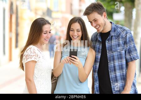 Tre amici felice controllo smart phone contenuto in piedi in una strada Foto Stock