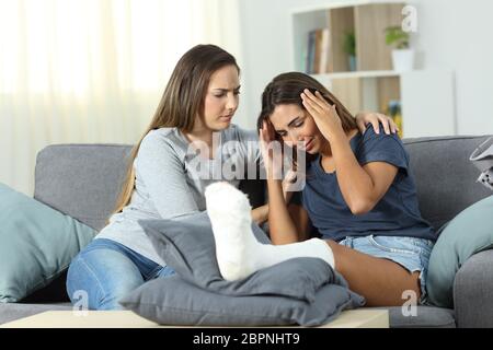 Triste donna disabile e amico e consolante la sua seduta su un divano nel salotto di casa Foto Stock