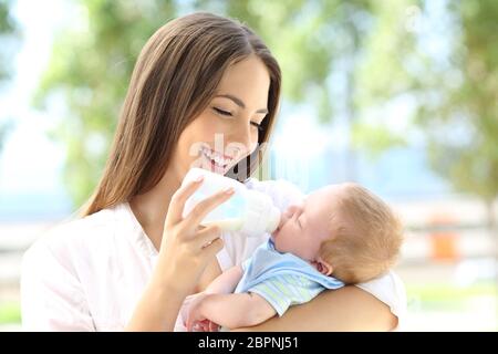 Ritratto di una madre felice di dare biberon al suo bambino all'aperto Foto Stock