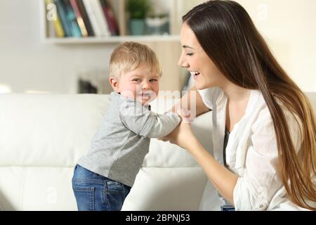 Madre aiutando a stare a suo figlio che ti guarda su un divano nel salotto di casa Foto Stock