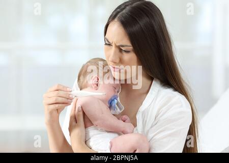 Madre di termometro di controllo mentre tiene il suo bambino malato a casa Foto Stock