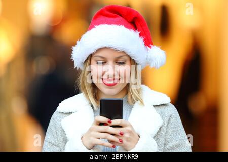 Ritratto di una ragazza felice che invia messaggi con smartphone durante le vacanze di natale per strada Foto Stock