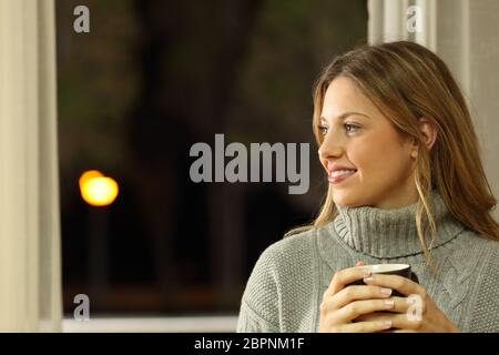 Ritratto di una donna penosa che guarda il lato tenendo una tazza di caffè a casa nella notte Foto Stock