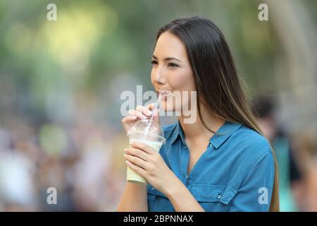 Donna felice sorseggiando milk shake a piedi in strada Foto Stock