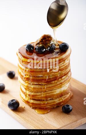 American dolce casalingo pila di pancake o le frittelle con mirtillo Frutta, noci e miele, deliziosi dessert per colazione, su sfondo bianco. Sel Foto Stock