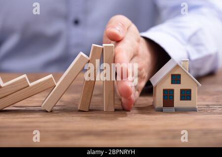 Close-up della mano umana proteggere Rosa Piggybank dalla caduta dei blocchi di legno sulla scrivania Foto Stock