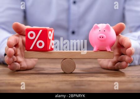 Mano umana la protezione di equilibrio tra Red percentuale Blocco cubico e Piggybank su altalena in legno Foto Stock