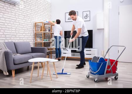 Vista laterale di due persone la pulizia del ripiano e pavimento con straccio nel soggiorno Foto Stock