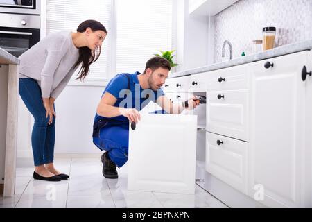 Donna che guarda la tuttofare maschio Installazione sportello di armadietto in cucina Foto Stock