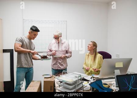 I colleghi sono di celebrare un compleanno in ufficio e sono ripartire la torta al cioccolato. Foto Stock
