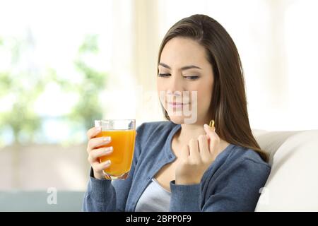 Donna dubitare tra vitamina pillola o succo di arancia seduti su un divano nel salotto di casa Foto Stock