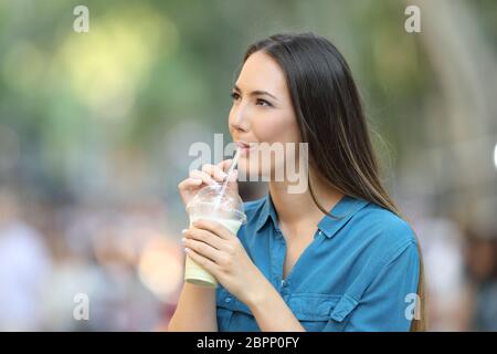 Donna felice di bere un smoothie guardando a lato su strada Foto Stock