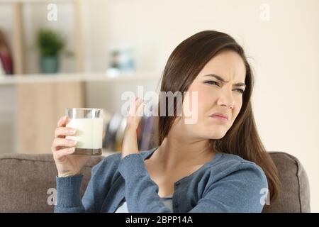 La donna che rifiuta un bicchiere di latte seduta su un divano nel salotto di casa Foto Stock