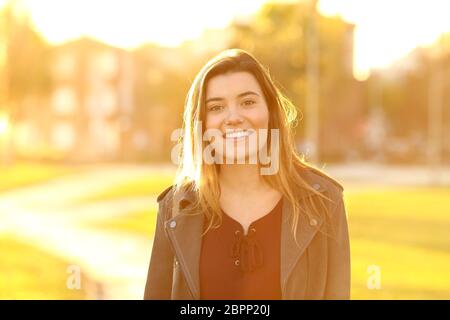 Vista anteriore verticale di un felice ragazza adolescente guardando la fotocamera in un parco al tramonto Foto Stock