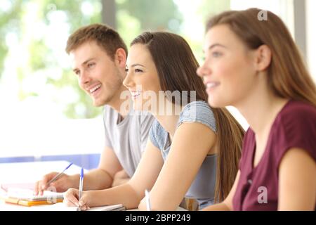 Vista laterale di tre felice attento ascolto gli studenti di una classe in una classe Foto Stock