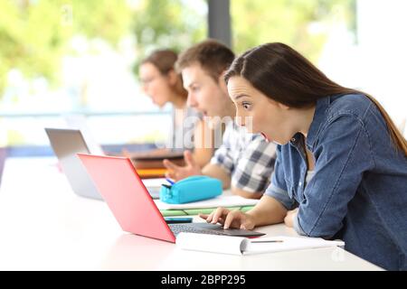 Vista laterale di tre stupiti gli studenti che ricevono buone notizie on line in una classe Foto Stock