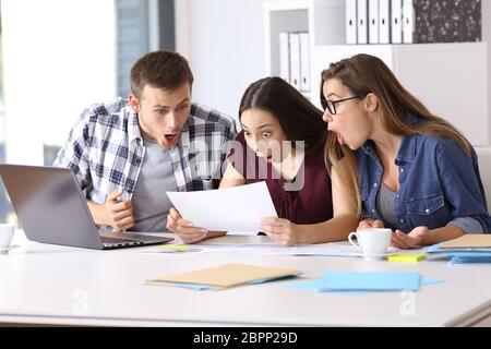 Tre dipendenti stupito la lettura di un documento cartaceo in ufficio Foto Stock