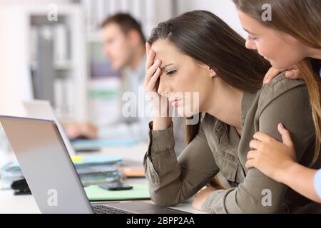 Triste dipendente riceve cattive notizie sulla linea essendo confortato da un collega in ufficio Foto Stock