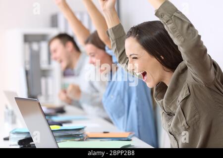Tre dipendenti eccitati ricevendo buone notizie on line nei notebook in ufficio Foto Stock