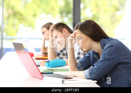 Vista laterale di tre studenti frustrato cercando di imparare on line in aula con uno sfondo verde Foto Stock