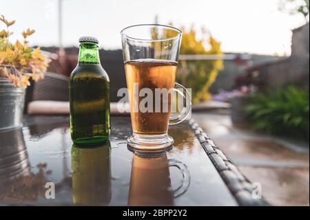 Birra fresca versata in vetro sul tavolo da giardino che si affaccia sul paesaggio del giardino in una profondità di campo poco profonda, sfondo sfocato. Foto Stock