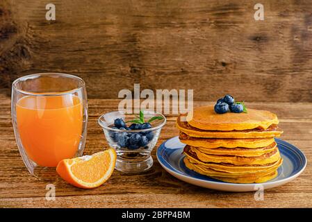 Un mucchio di pancake di zucca con mirtilli e succo d'arancia su rustico fondo di legno. Spazio di copia. Foto Stock