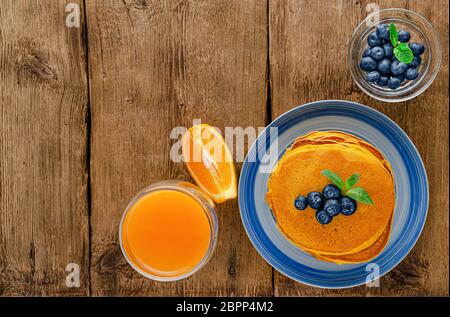 Pancake di zucca con mirtilli e succo d'arancia su rustico sfondo di legno. Spazio di copia. Overhead Foto Stock