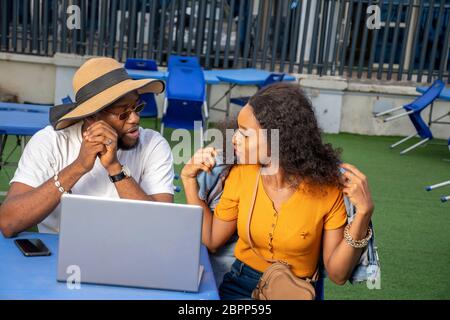 due giovani neri seduti insieme all'aperto con un computer portatile, che hanno una discussione Foto Stock