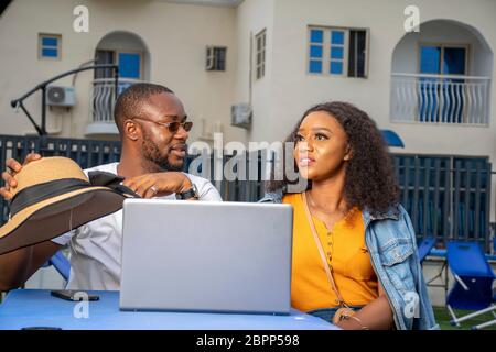 giovane uomo nero e donna seduti insieme all'aperto con un computer portatile, facendo una discussione Foto Stock