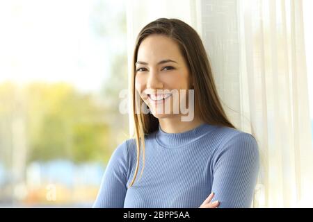 Ritratto di un felice proprietario di abitazione guardando la fotocamera accanto a una finestra a casa Foto Stock