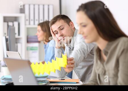 Ritratto di un dipendente pigro noioso seduti in un desktop tra gli altri lavoratori in ufficio Foto Stock