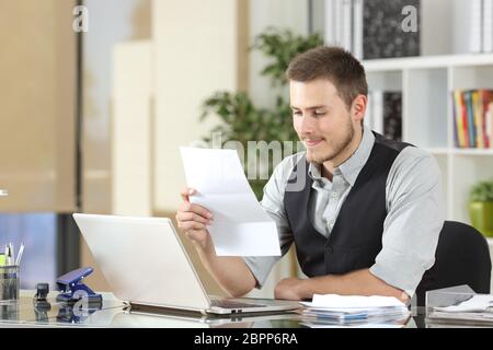 Happy businessman la lettura di una lettera seduto in una scrivania in ufficio Foto Stock