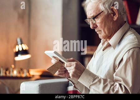 Uomo anziano da solo seduto alla biblioteca guardando la foto di pensiero primo piano Foto Stock
