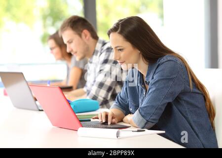 Vista laterale di tre studenti attenti e-learning sulla linea di notebook con seduta in aula Foto Stock