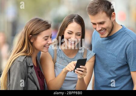 Tre amici felici che controllano i contenuti dello smartphone in piedi fuori dalla strada Foto Stock