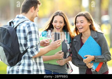 Tre studenti di felice condivisione smart phone contenuto in un parco Foto Stock