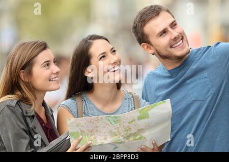 Tre turisti felici che tengono una mappa godendo le vacanze in piedi sulla strada Foto Stock