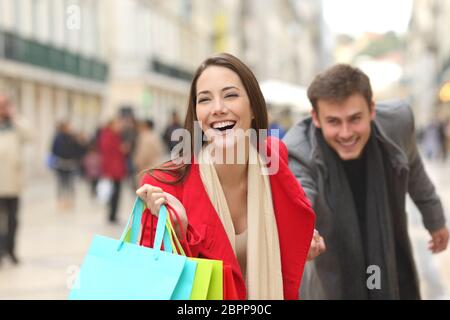 Vista frontale di un casual giovane di acquirenti in esecuzione nella strada verso la telecamera tenendo colorato borse per lo shopping Foto Stock