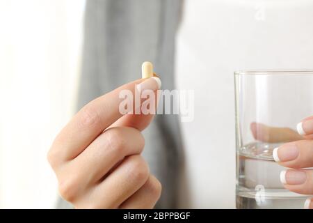 Primo piano di una mano di ragazza che tiene una pillola e un bicchiere d'acqua Foto Stock