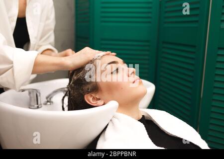 Bella ragazza giovane lava la testa in uno studio di bellezza. Il parrucchiere è lavare i capelli per il cliente Foto Stock