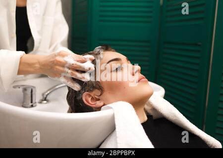 Bella ragazza giovane lava la testa in uno studio di bellezza. Il parrucchiere è lavare i capelli per il cliente Foto Stock