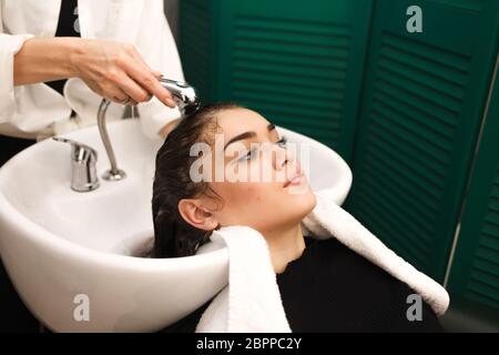 Bella ragazza giovane lava la testa in uno studio di bellezza. Il parrucchiere è lavare i capelli per il cliente Foto Stock