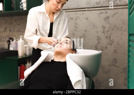 Bella ragazza giovane lava la testa in uno studio di bellezza. Il parrucchiere è lavare i capelli per il cliente Foto Stock